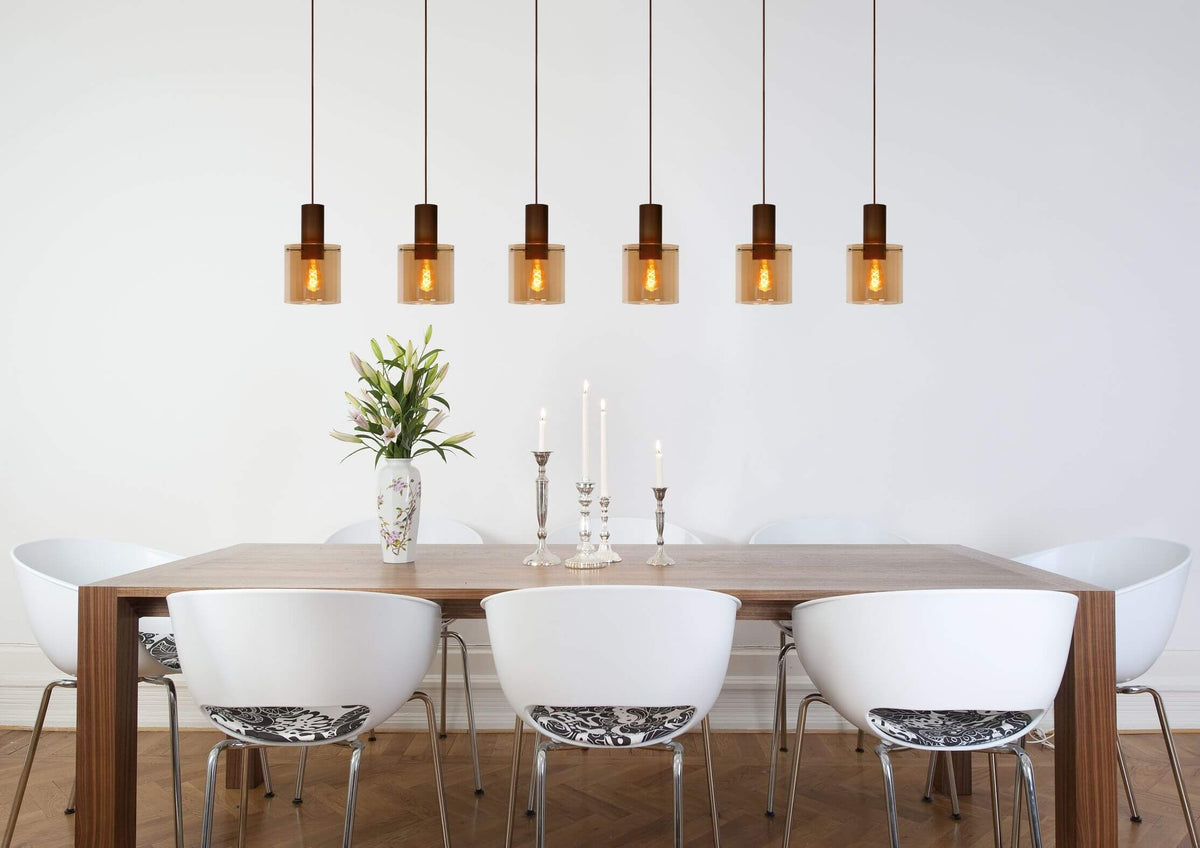 Plan large montrant une suspension aux multiples verres ambrés éclairant une table dressée de fleurs.