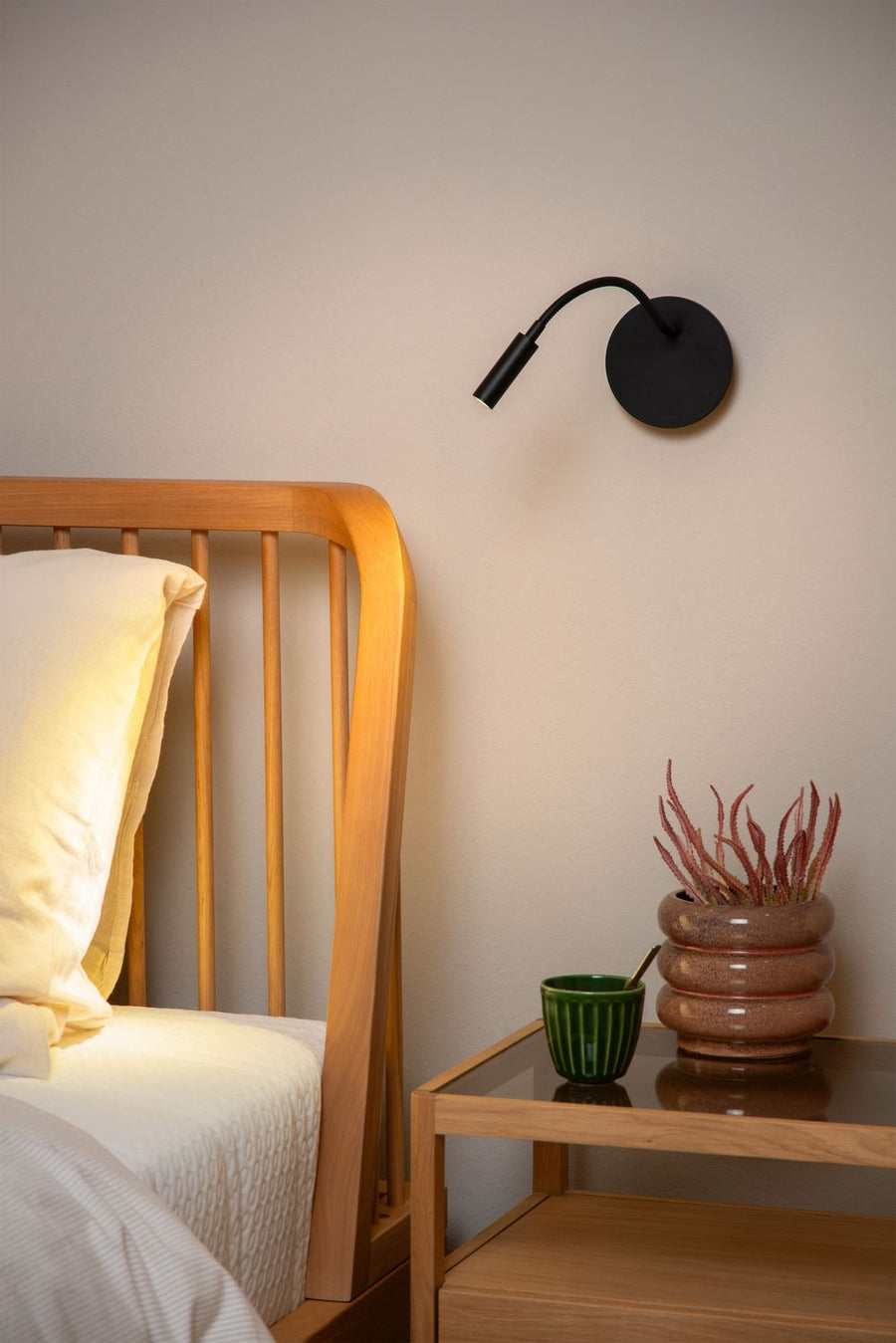 Vue rapprochée de l'applique murale noire installée près d'un lit en bois clair.
