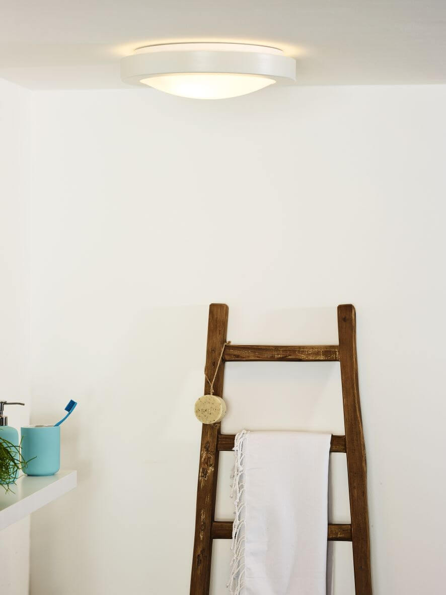 Plafonnier blanc allumé au plafond dans une salle de bain décorée, échelle en bois et serviette.