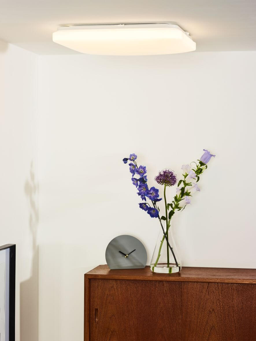 Plafonnier allumé fixé au plafond blanc au-dessus d'un meuble en bois et d'un vase de fleurs