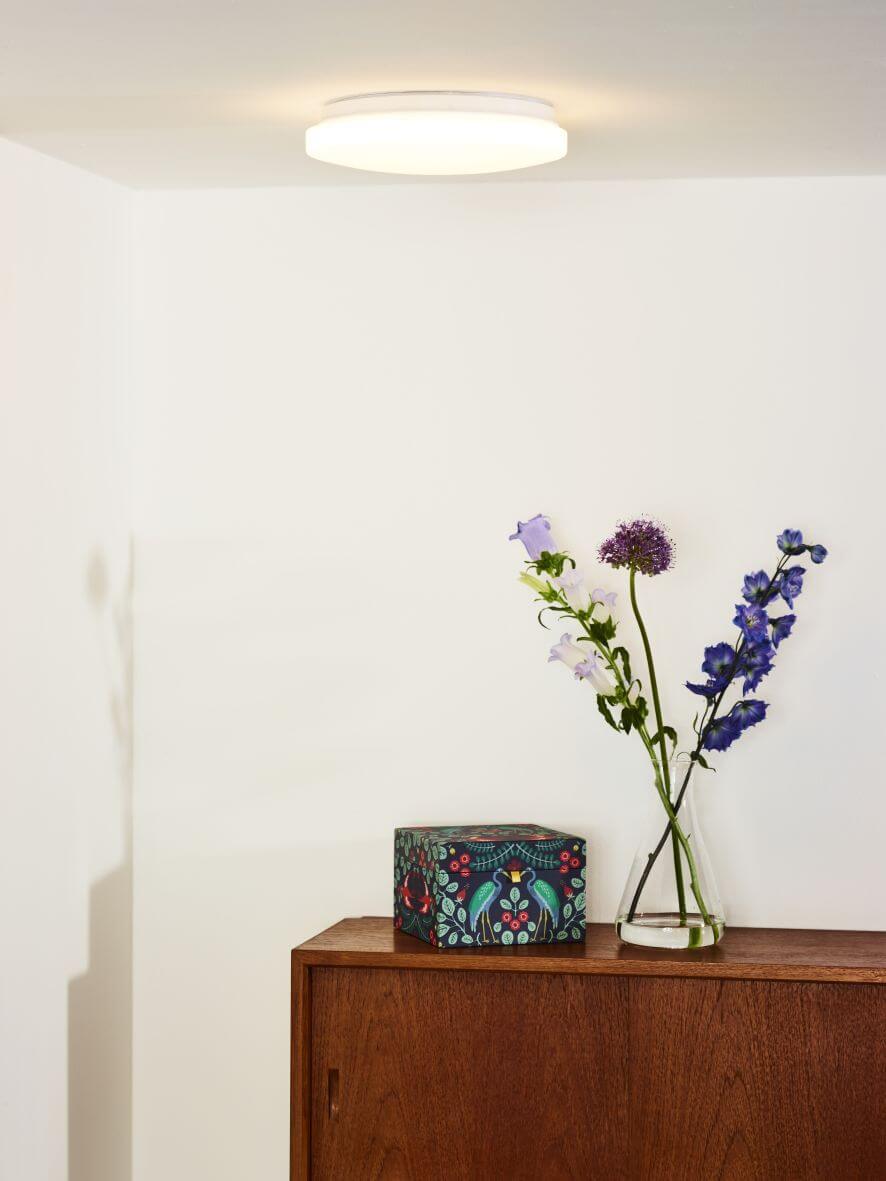 Plafonnier rond allumé au plafond d'une pièce blanche avec fleurs et meuble bois