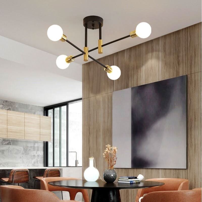 Luminaire fixé au plafond d'une salle à manger, bras noirs et dorés, globes blancs allumés.
