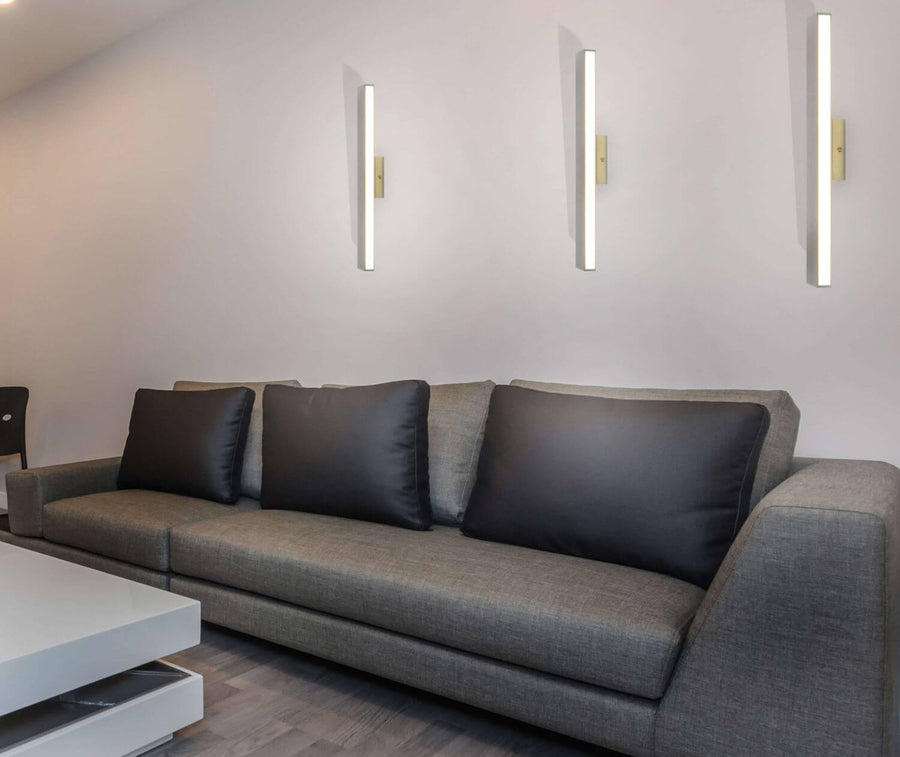 Trois appliques linéaires verticales allumées au-dessus d'un canapé gris en intérieur