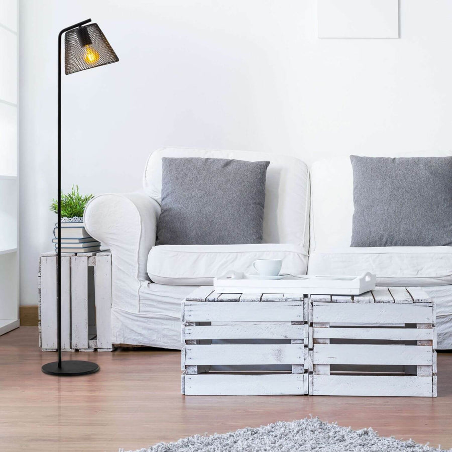 Lampadaire allumé près d'un canapé blanc, coussins gris et tables en caisses