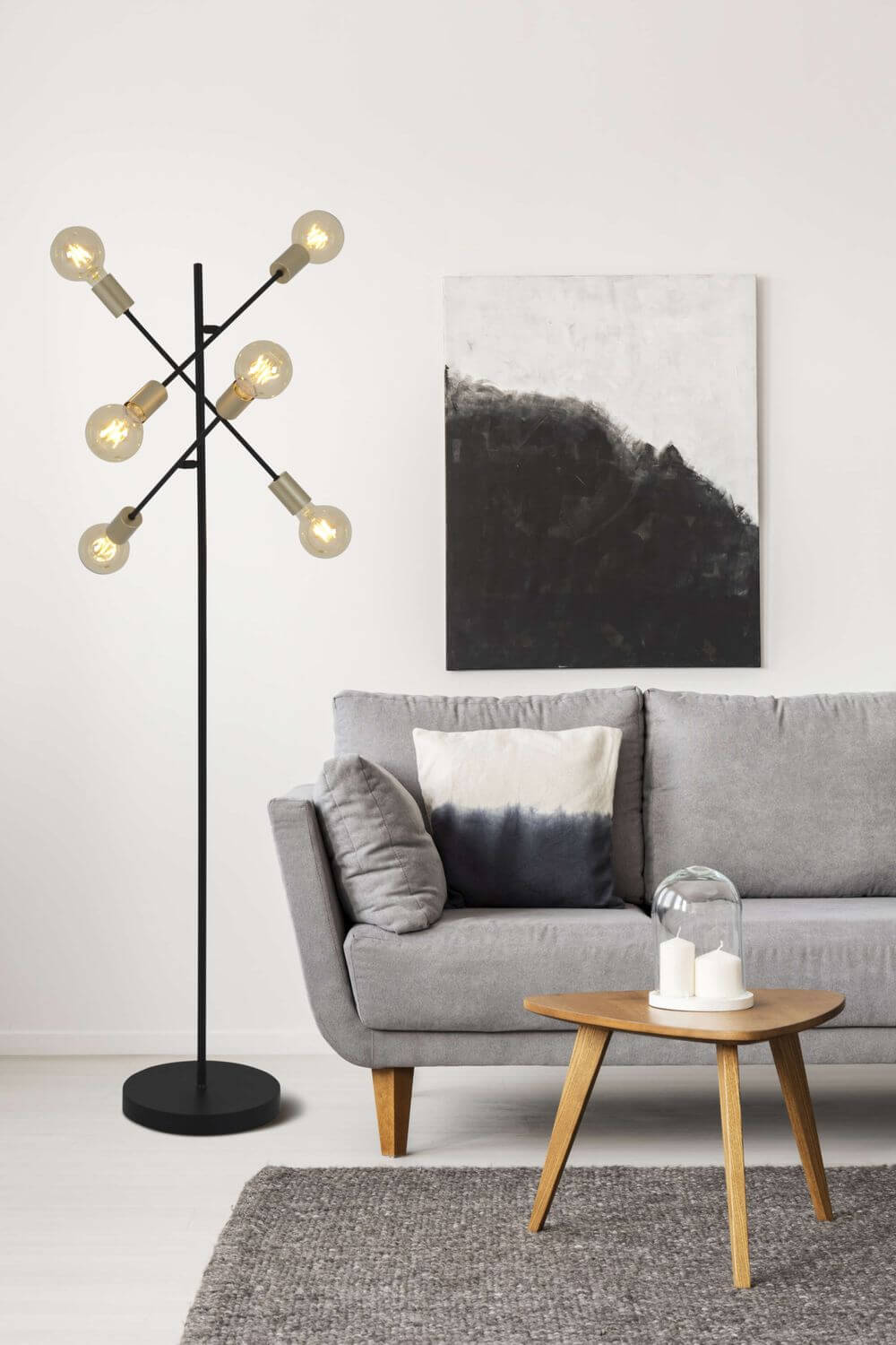 Lampadaire allumé en situation, près d'un canapé gris et d'un tableau abstrait