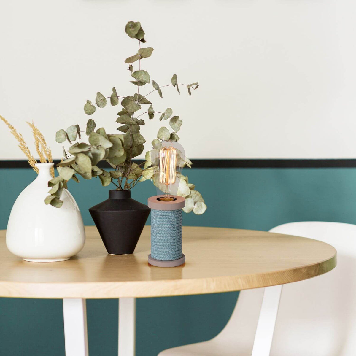 Mise en ambiance sur table en bois, lampe turquoise parmi vases et eucalyptus.