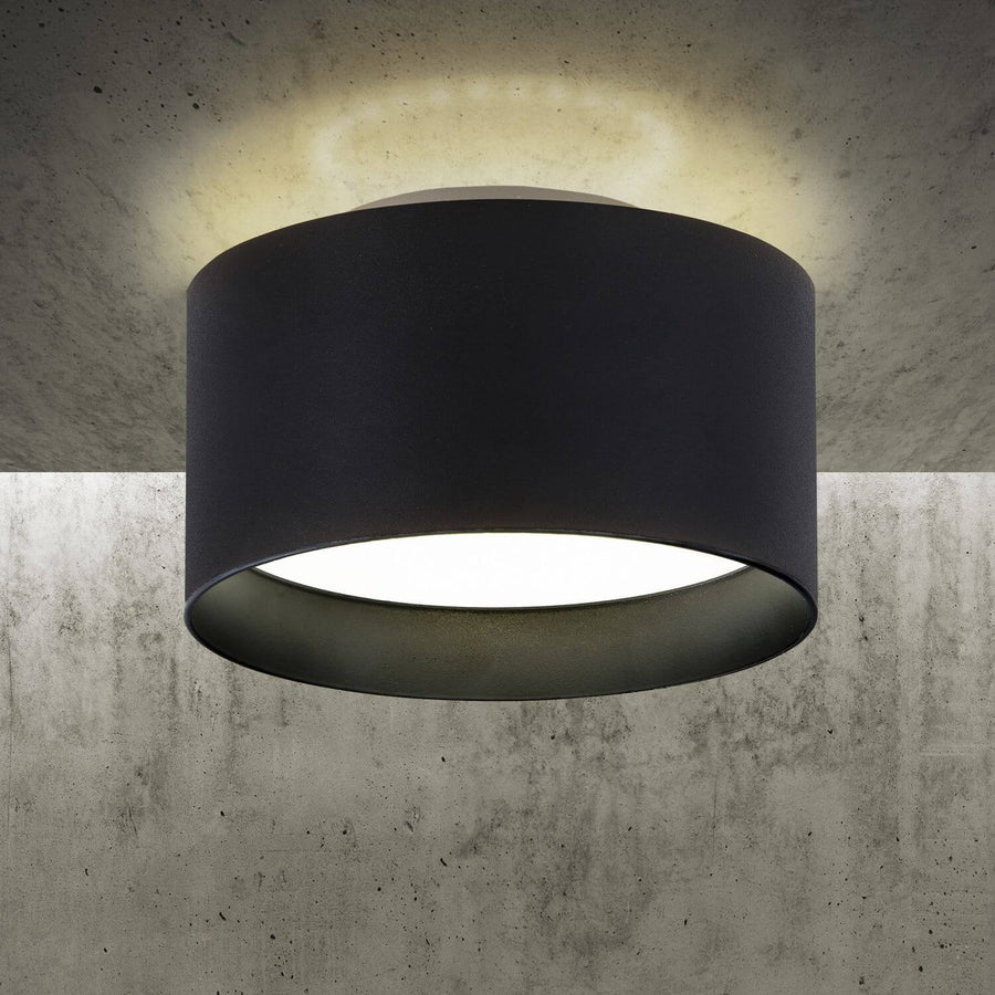 Gros plan du plafonnier allume projetant un halo sur un mur beton