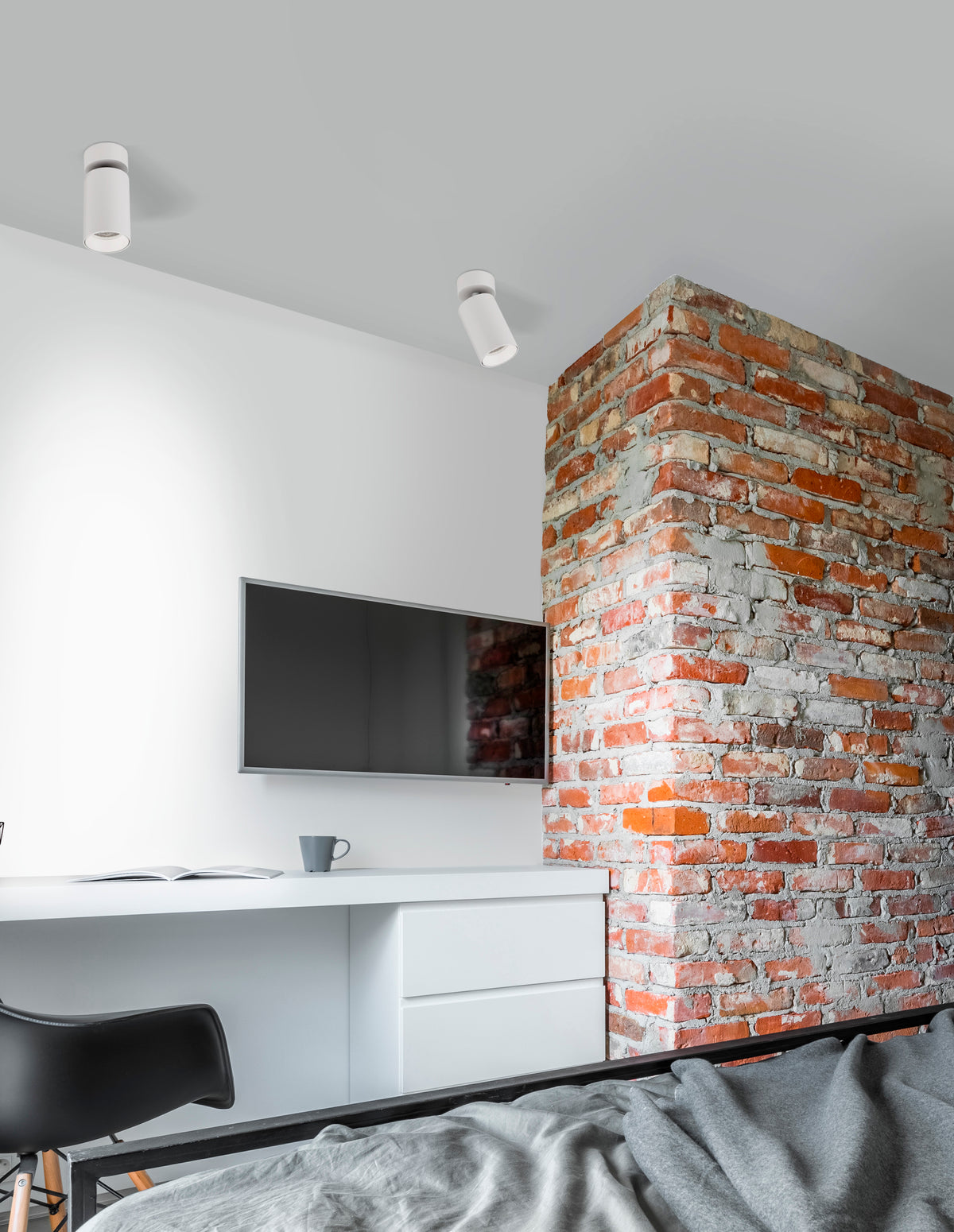 Mise en ambiance de deux plafonniers blancs orientables dans une chambre à mur de briques