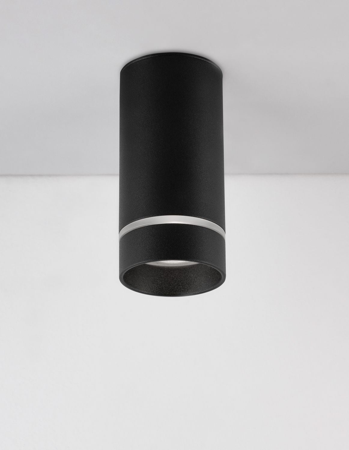 Plafonnier cylindrique noir monté au plafond, vu de trois quarts sur fond blanc.