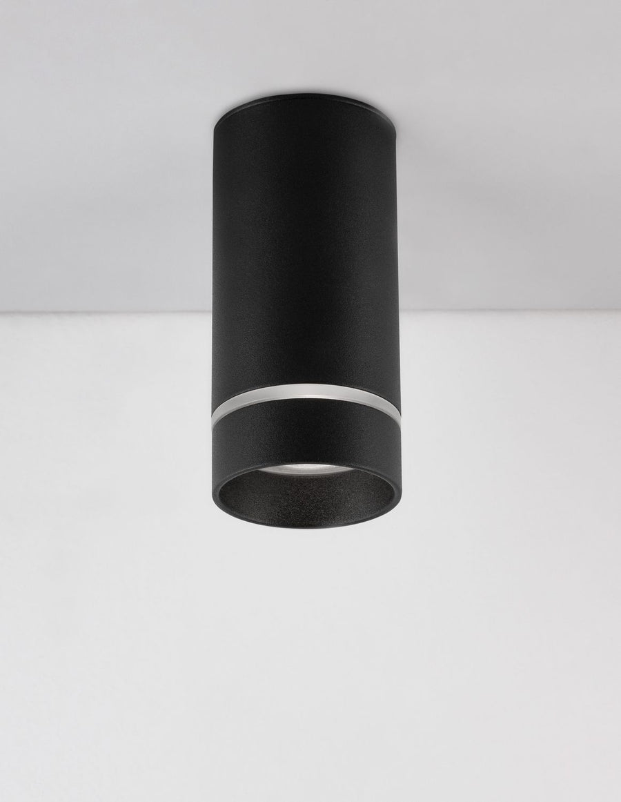 Plafonnier cylindrique noir monté au plafond, vu de trois quarts sur fond blanc.