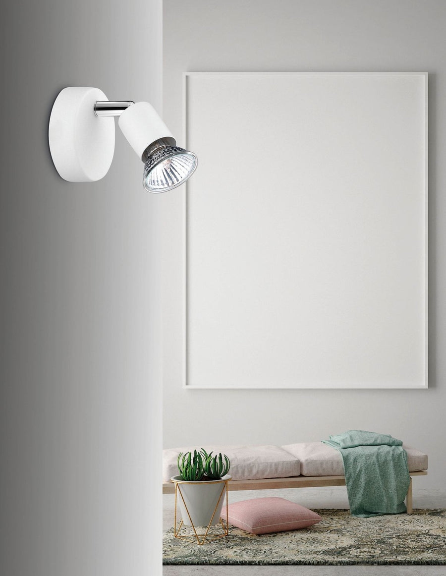 Luminaire blanc orientable fixé sur une cloison, au-dessus d'un banc dans un intérieur clair.