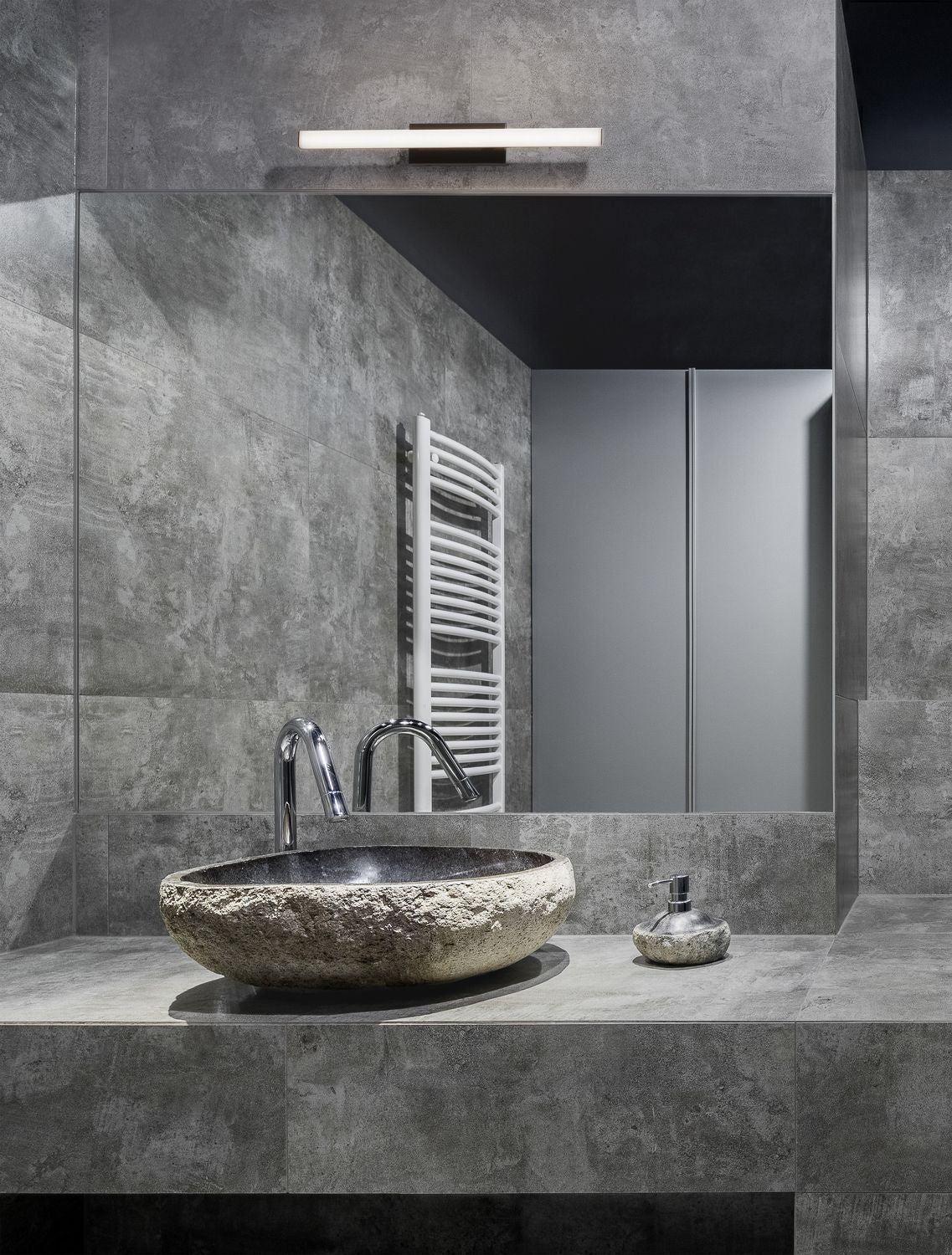 Applique murale noire allumée au-dessus d'un miroir de salle de bain en pierre grise