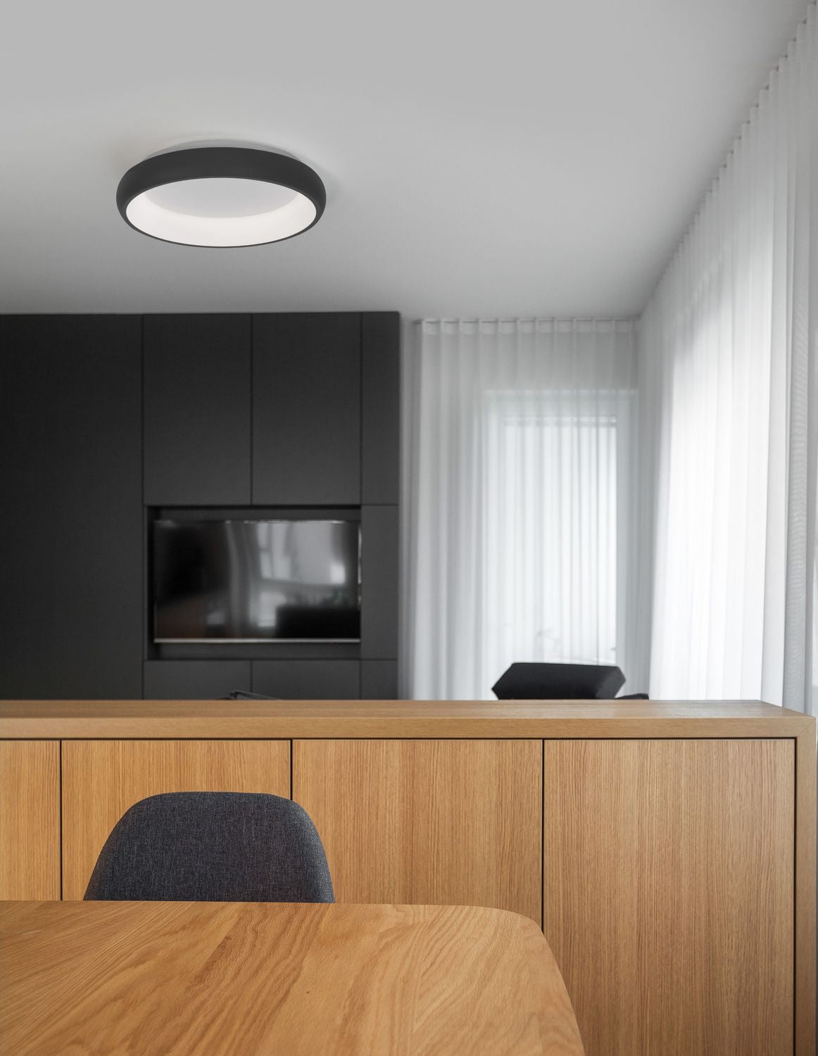 Plafonnier rond noir installé au plafond dans un intérieur bois et noir contemporain