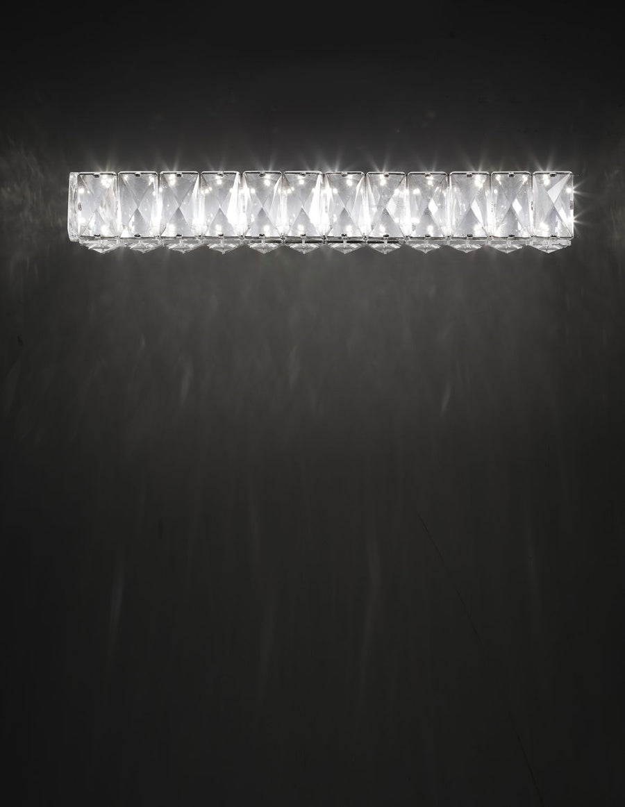 Applique murale en cristal allumée, halo lumineux projeté sur un mur sombre.