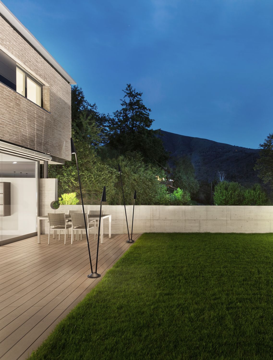 Ambiance du soir sur une terrasse en bois avec les luminaires allumés.