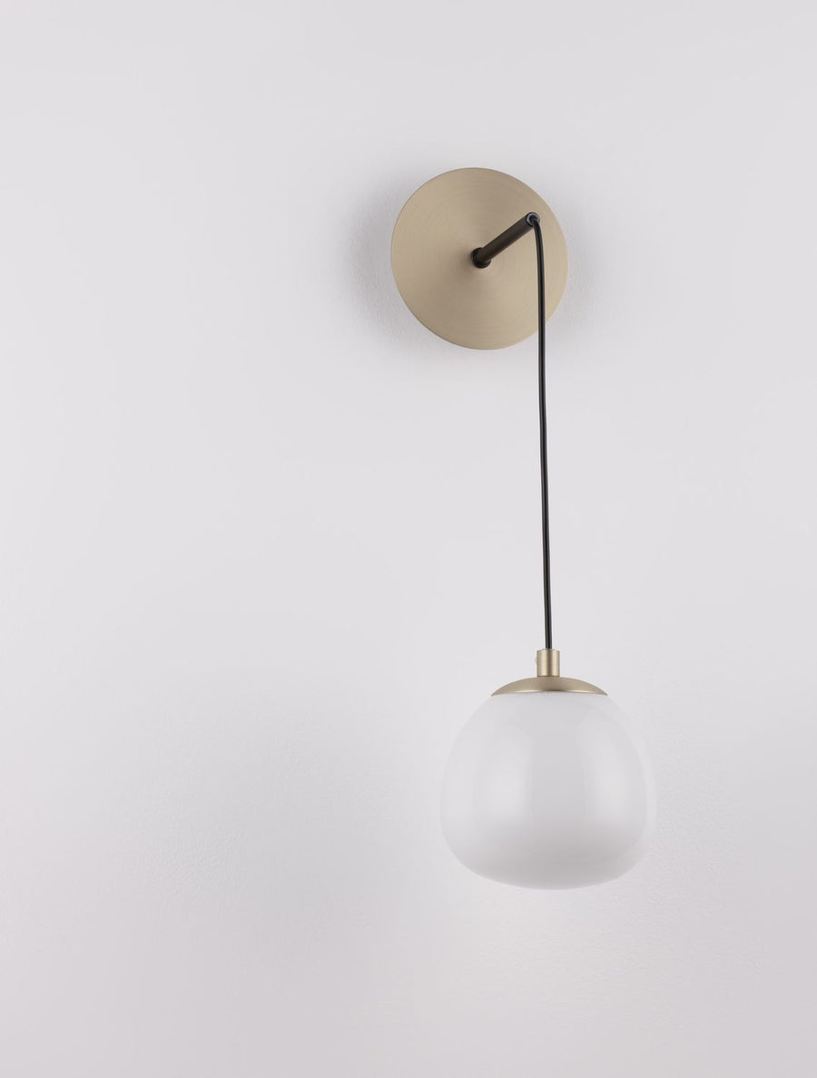 Applique fixée sur un mur blanc, platine dorée et câble noir vertical