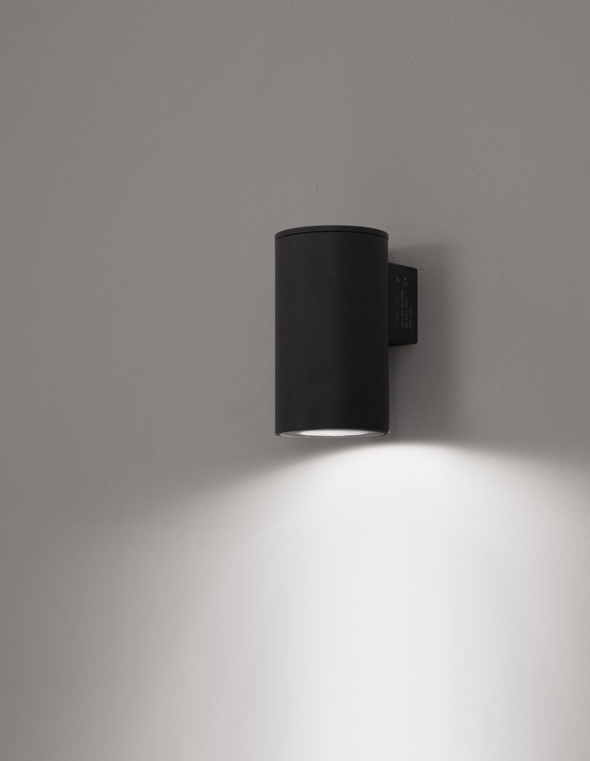 Applique murale noire allumée, halo de lumière projeté sur un mur blanc.