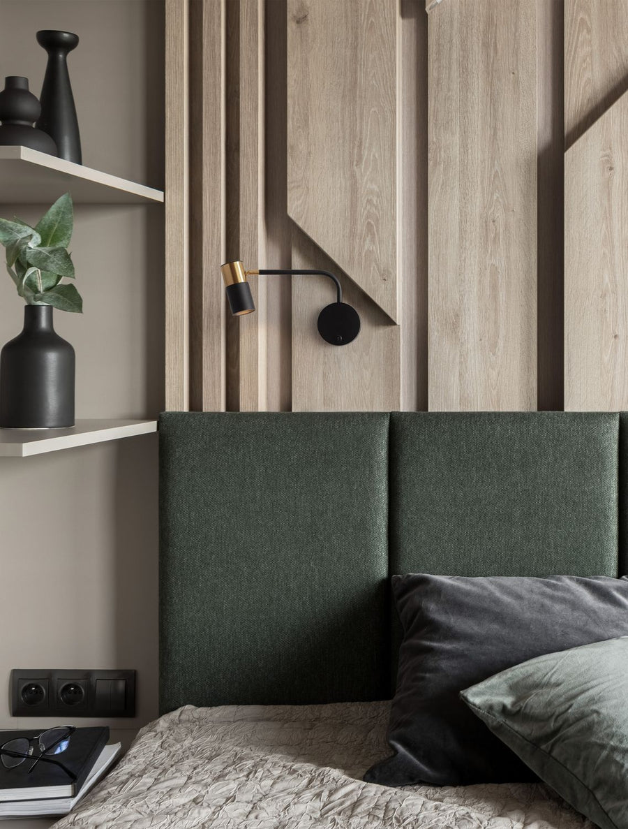 Applique murale noire et dorée installée au-dessus d'une tête de lit en bois clair