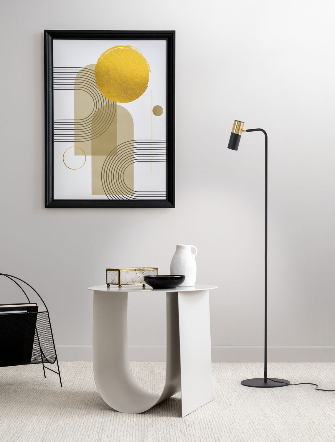 Mise en ambiance : lampadaire noir et doré devant un tableau doré, table basse blanche.