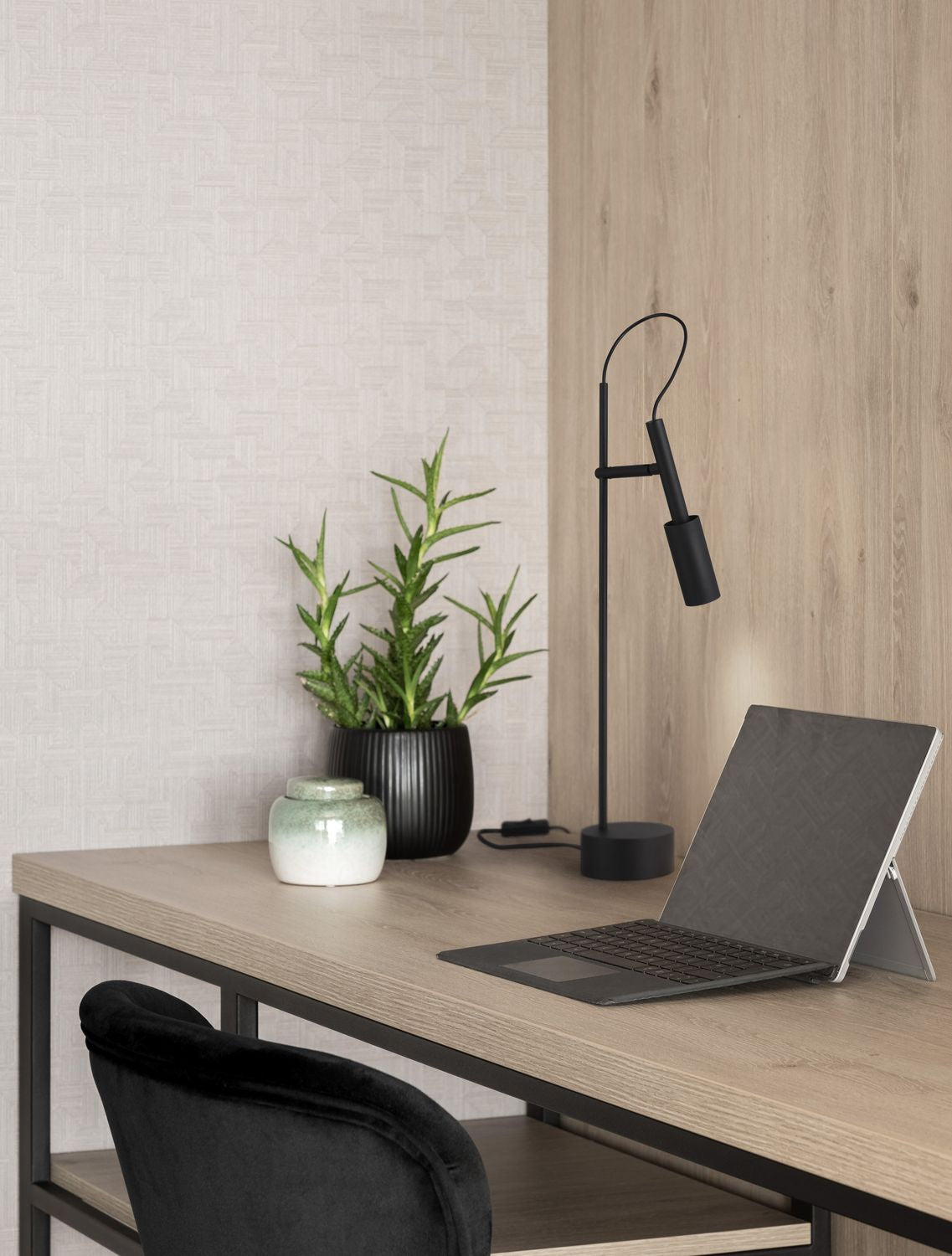 Lampe à poser noire sur un bureau en bois, mise en ambiance avec plante et ordinateur