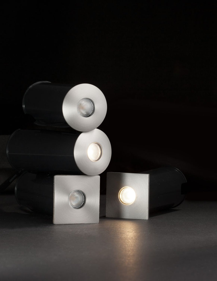 Trois luminaires encastrables posés sur fond noir, montrant versions rondes et carrées éclairées.