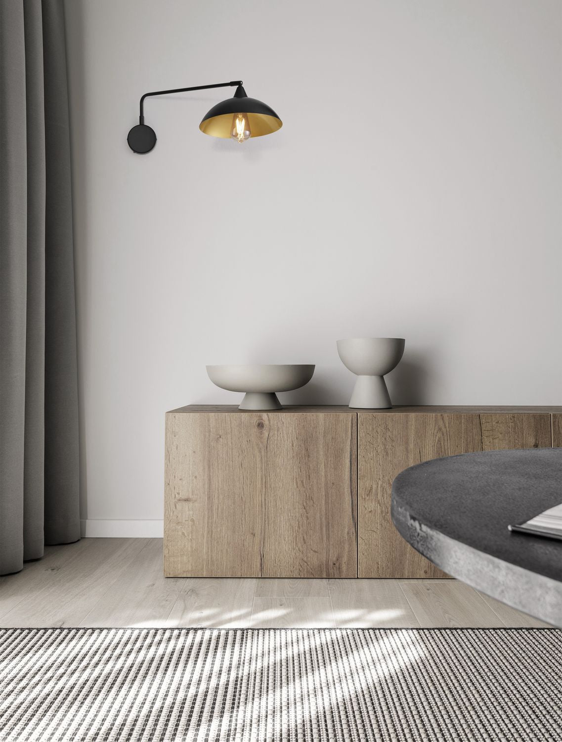 Mise en ambiance : applique murale noire allumée sur un mur clair au-dessus d'un meuble en bois