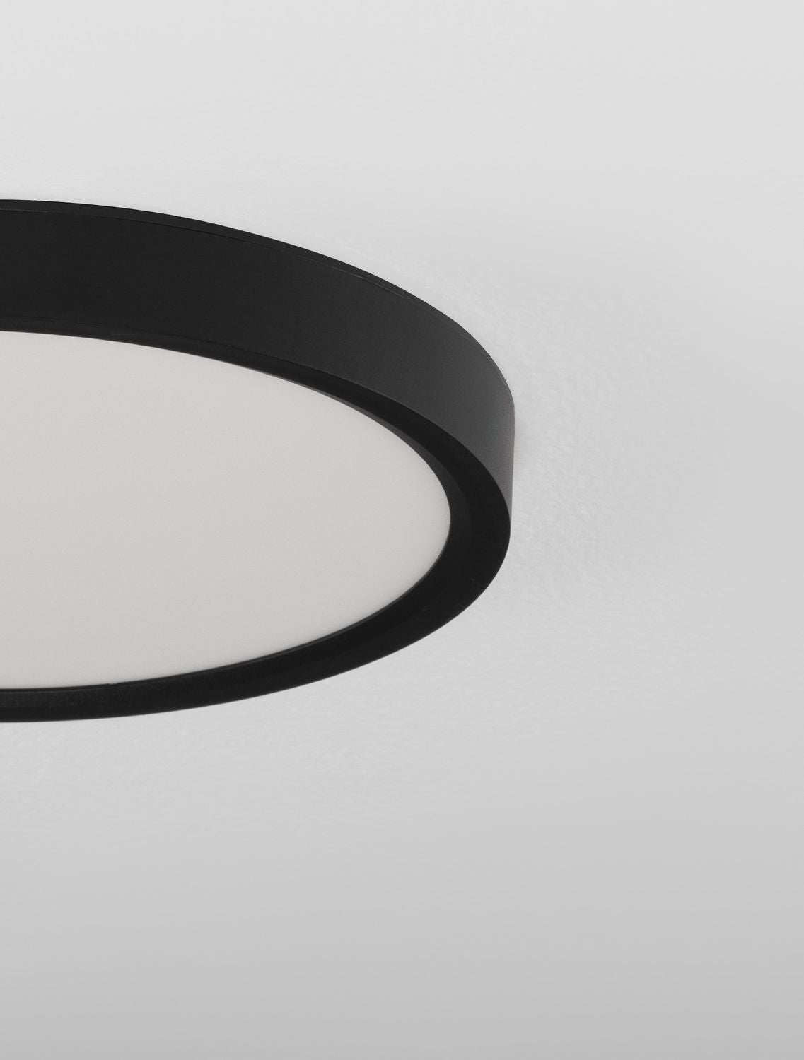 Gros plan sur le cerclage noir mat et le diffuseur blanc du plafonnier rond