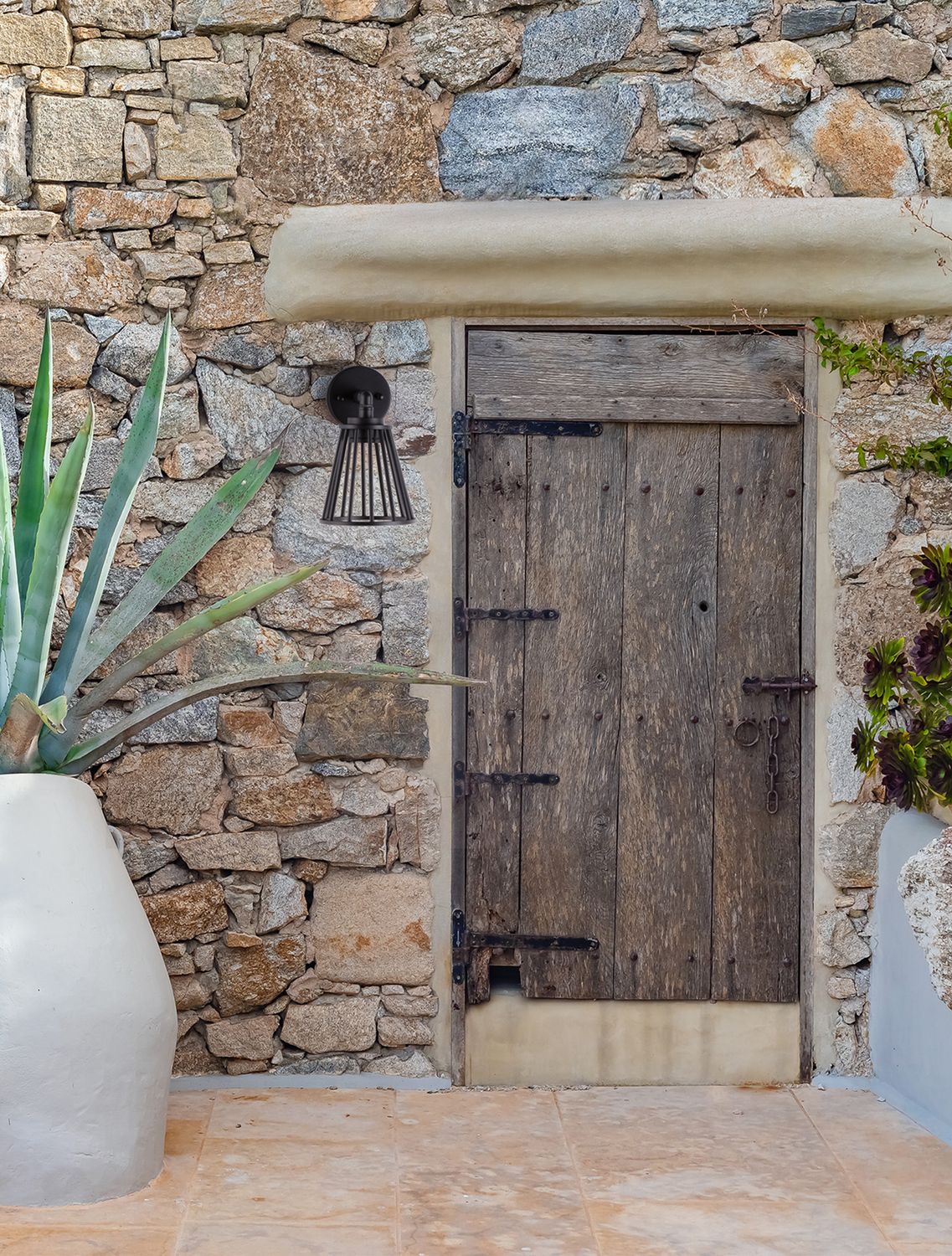 Applique noire fixée sur un mur en pierre, près d'une porte en bois ancienne