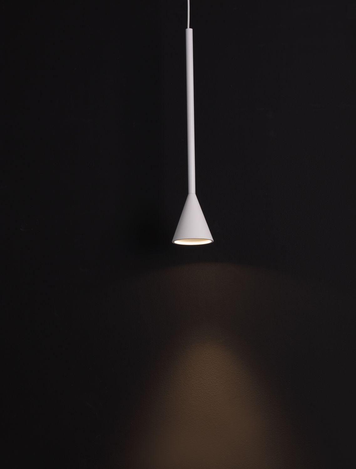 Luminaire blanc suspendu sur fond noir, faisceau lumineux projeté vers le sol