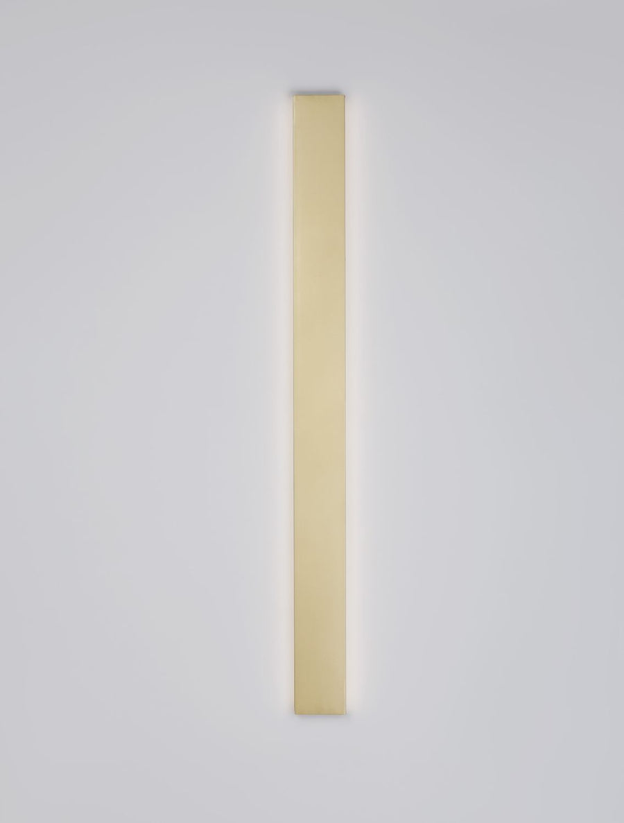 Luminaire vertical doré allumé, halo lumineux diffus sur le mur