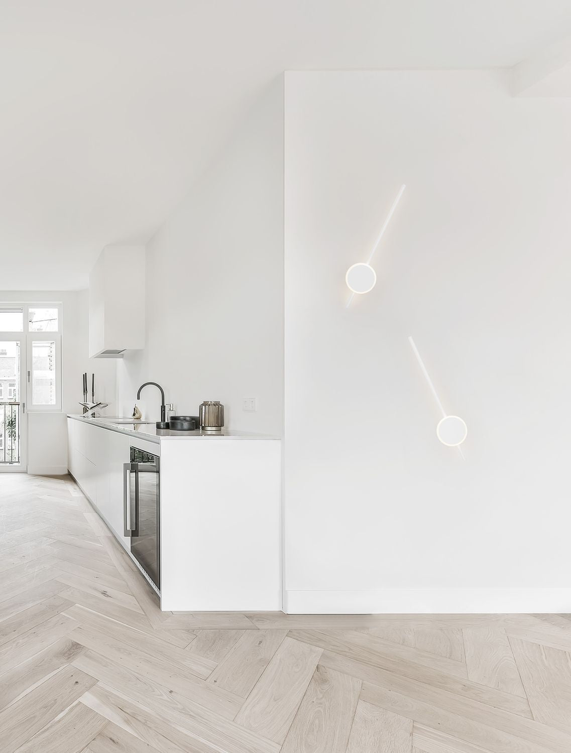 Vue d'ambiance d'une cuisine blanche avec deux appliques murales allumées fixées au mur