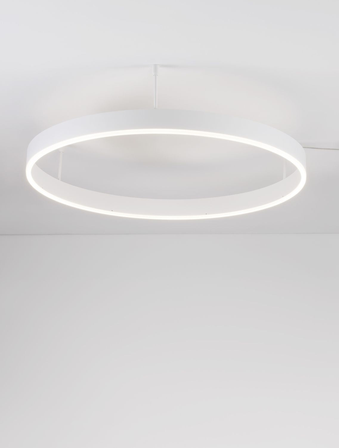 Vue en contre-plongée du luminaire allumé, montrant l'anneau blanc et la lumière diffuse vers le bas.