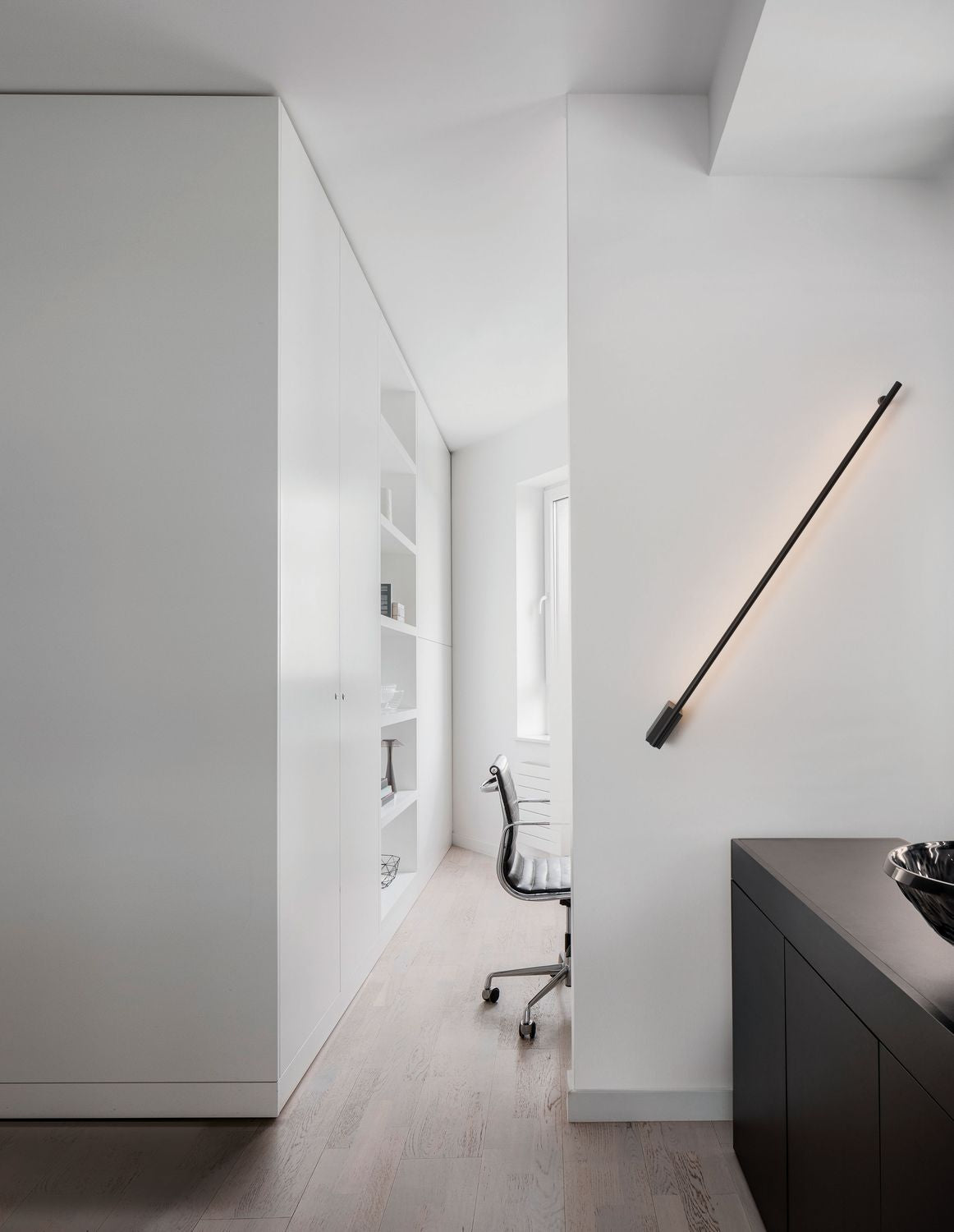 Applique murale noire diagonale éclairant un mur blanc dans un bureau épuré