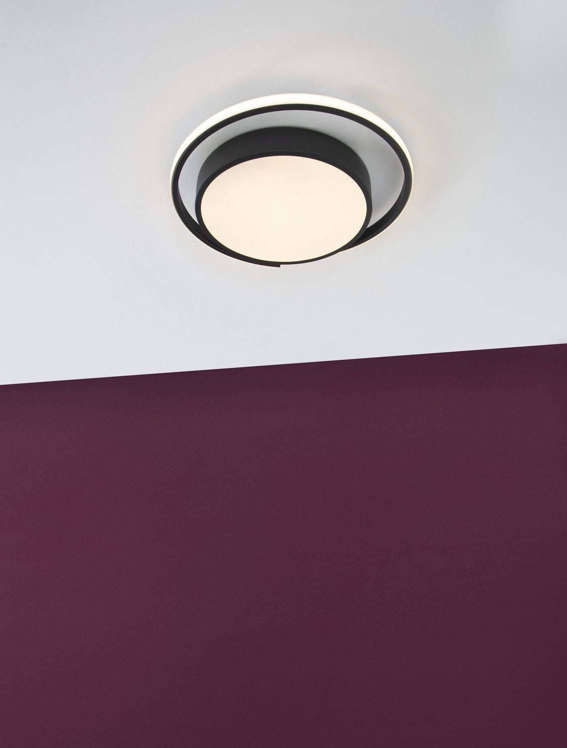Luminaire allumé fixé au plafond, mis en ambiance sur un mur violet.