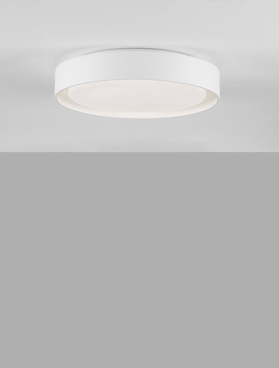 Gros plan sur le luminaire blanc rond allumé, bord cylindrique et diffuseur opale.