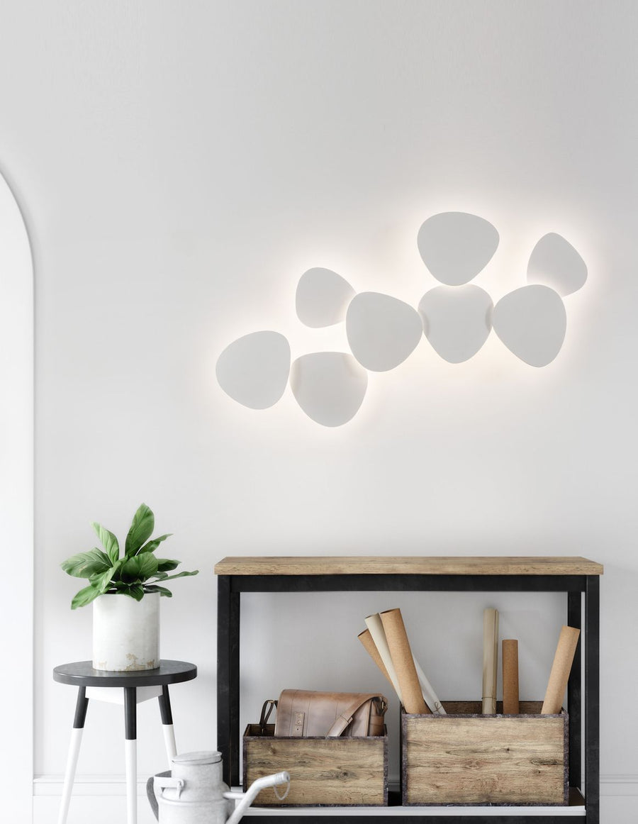 Applique murale blanche composée de sept modules sur un mur clair au-dessus d'un meuble en bois