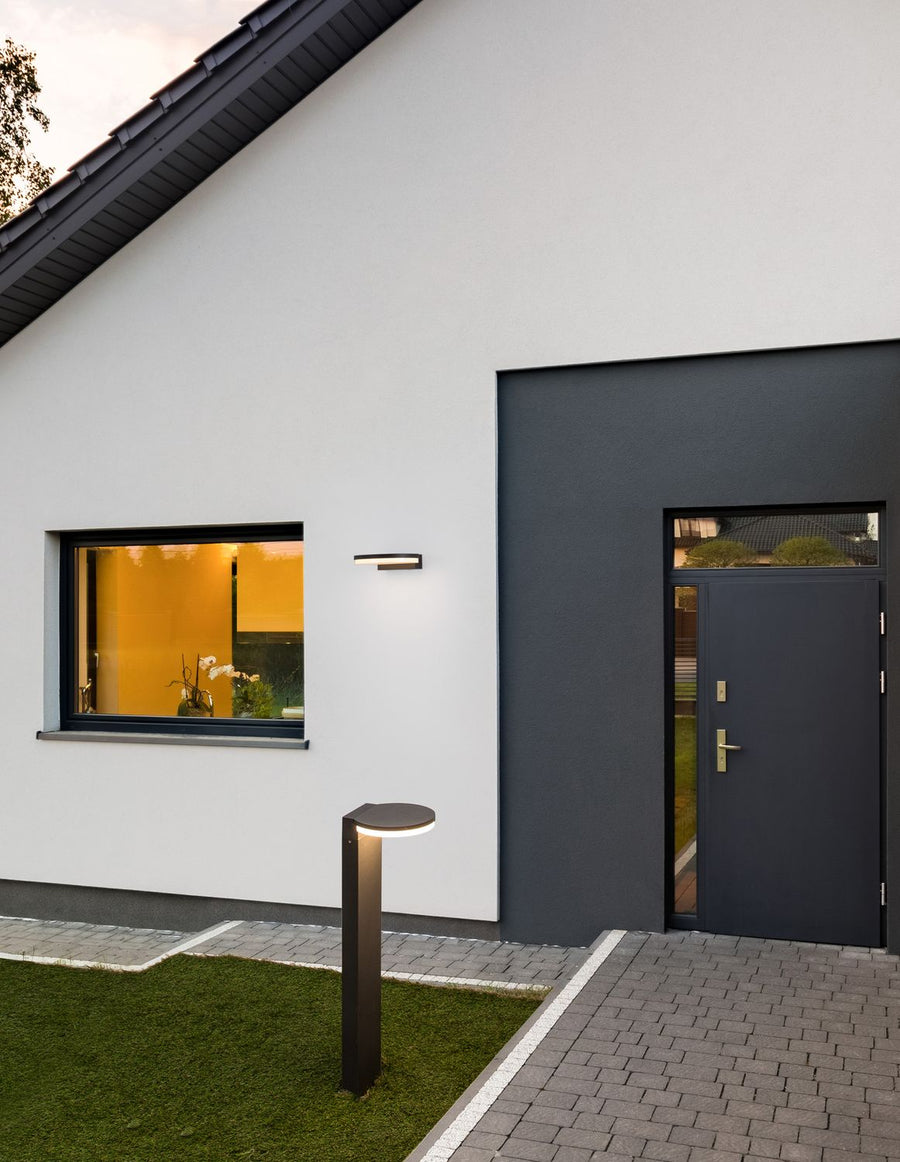 Borne anthracite installée dans un jardin devant une façade blanche et grise