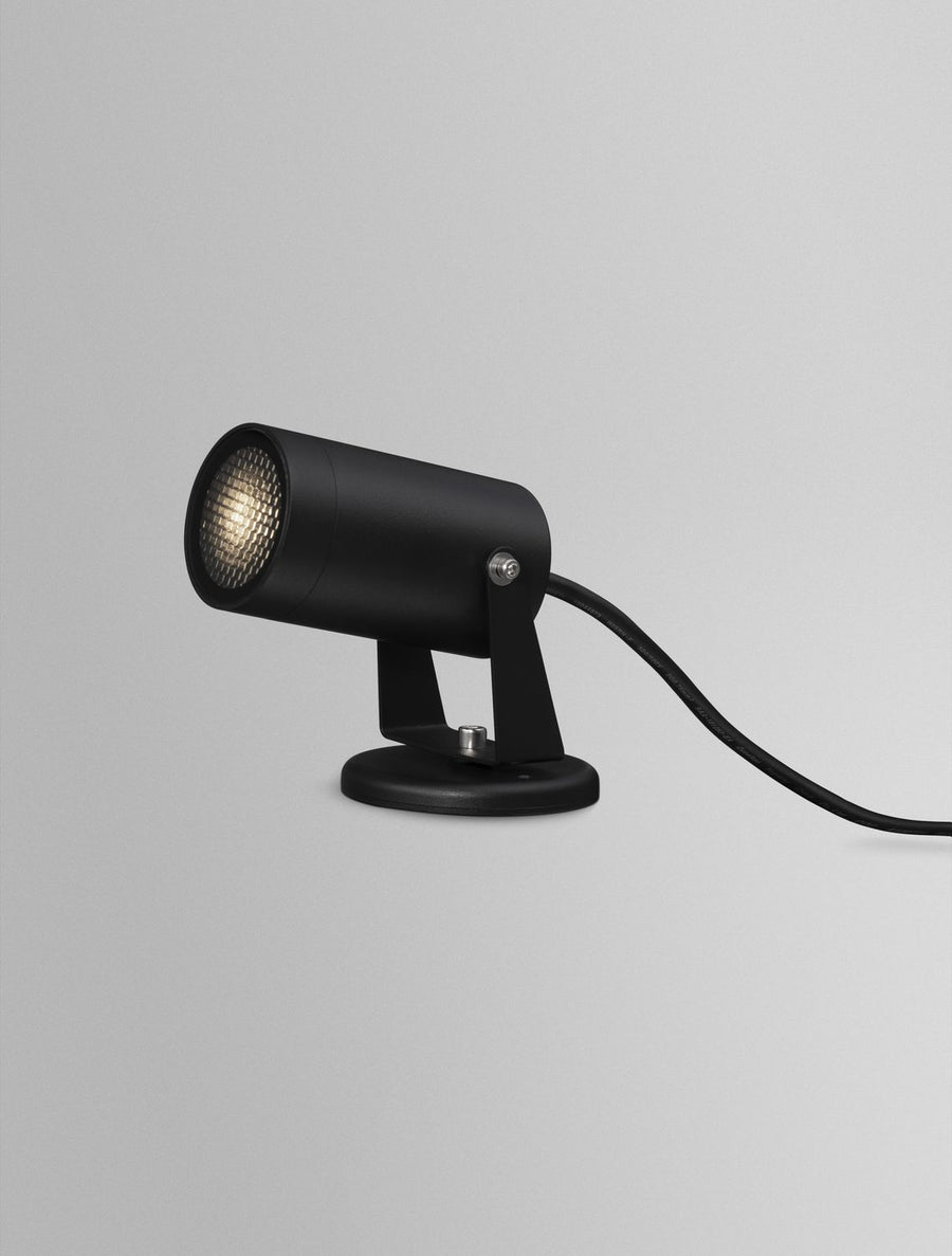 Projecteur noir allumé, lentille striée diffusant une lumière chaude en studio