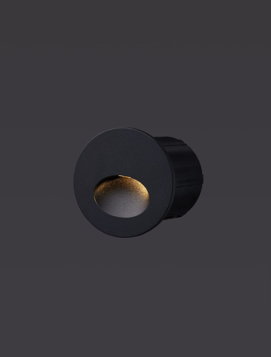 Luminaire encastré noir allumé, diffusant une lumière chaude dans son ouverture.