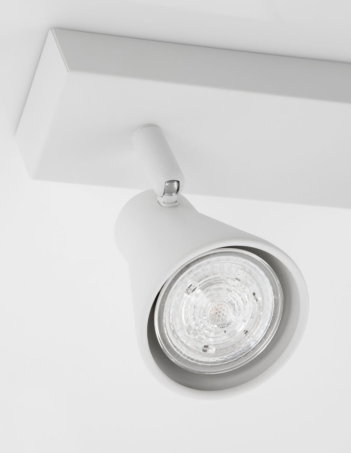 Détail d'un projecteur blanc avec lentille en verre et articulation chromée.