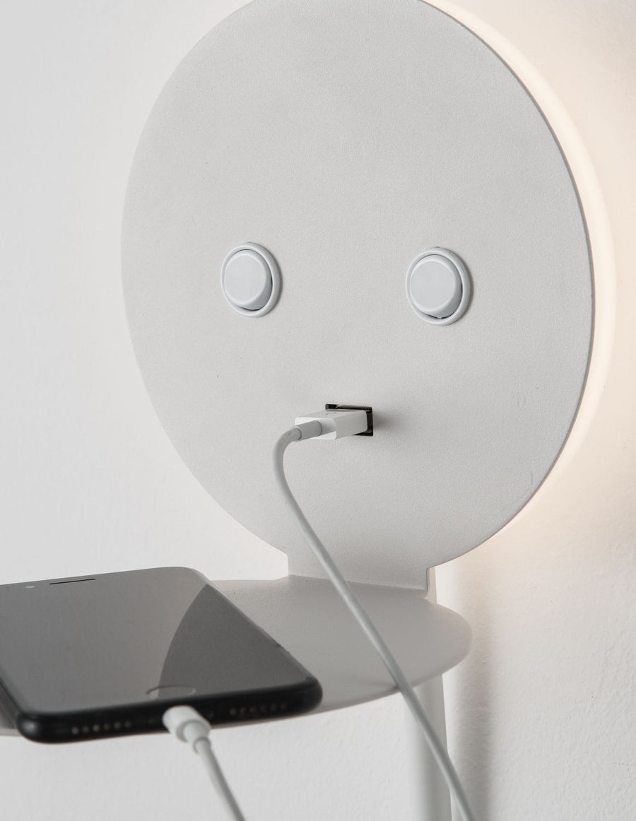 Gros plan sur une applique murale blanche avec téléphone en charge et port USB.