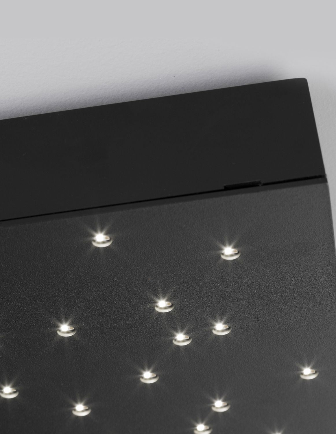 Vue rapprochée des points lumineux LED étoilés sur la face noire du plafonnier.