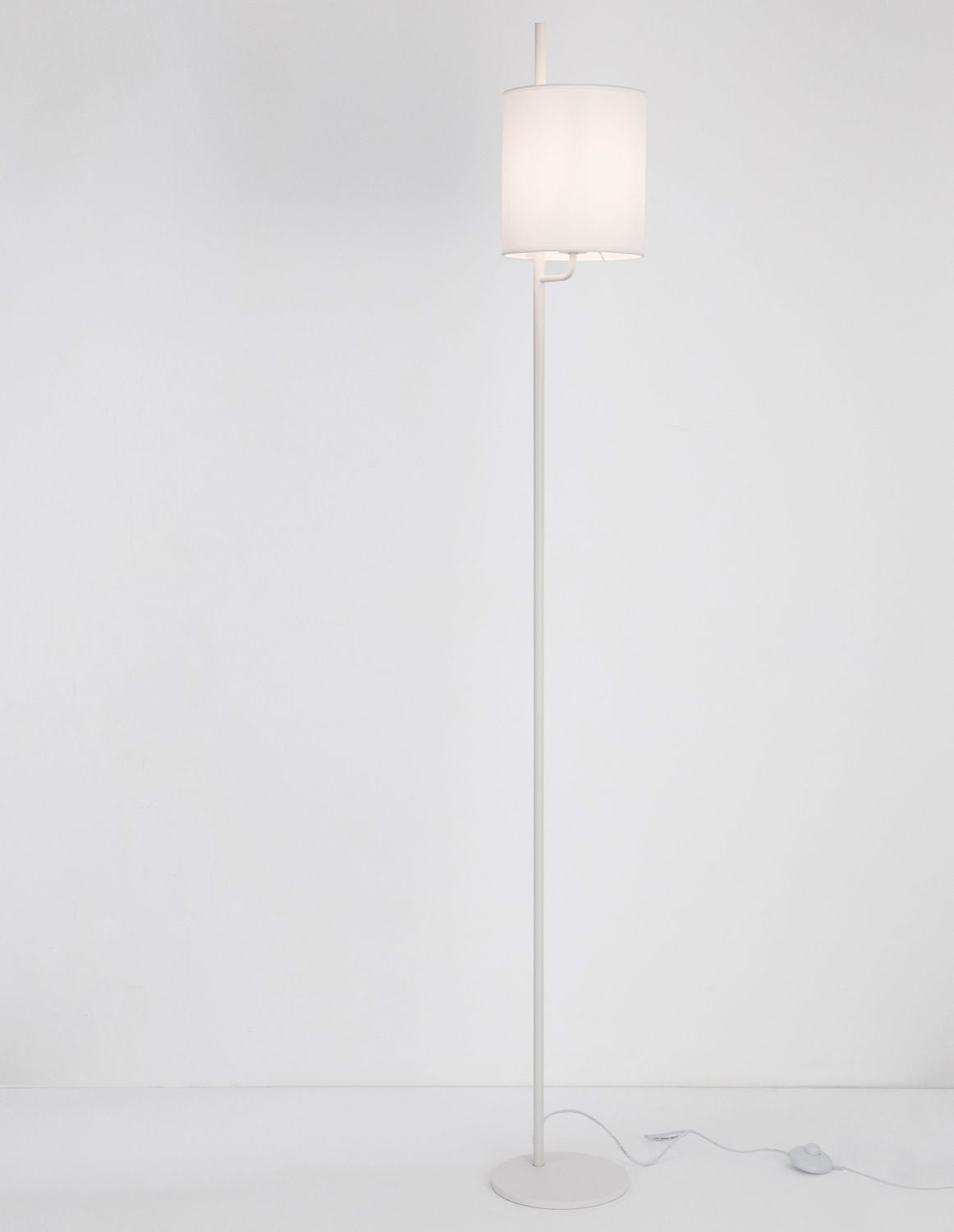 Lampadaire blanc de face avec abat-jour cylindrique en tissu, pied fin et câble.