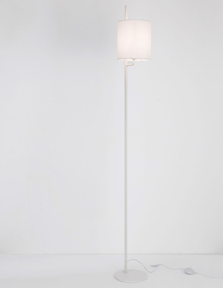 Lampadaire blanc de face avec abat-jour cylindrique en tissu, pied fin et câble.