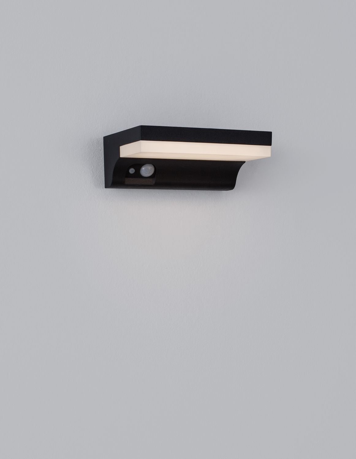 Applique éteinte fixée sur un mur gris clair, face avant avec détecteur.