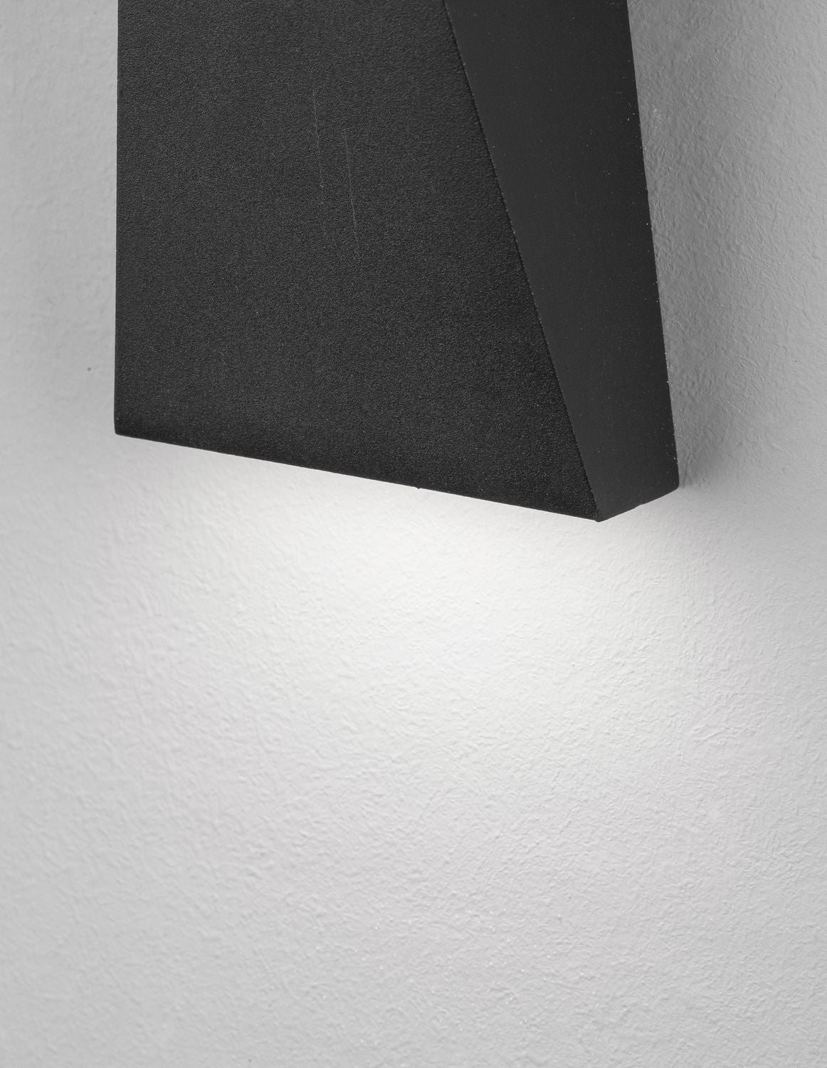 Détail du bas du luminaire noir et de la lumière rasante sur le mur