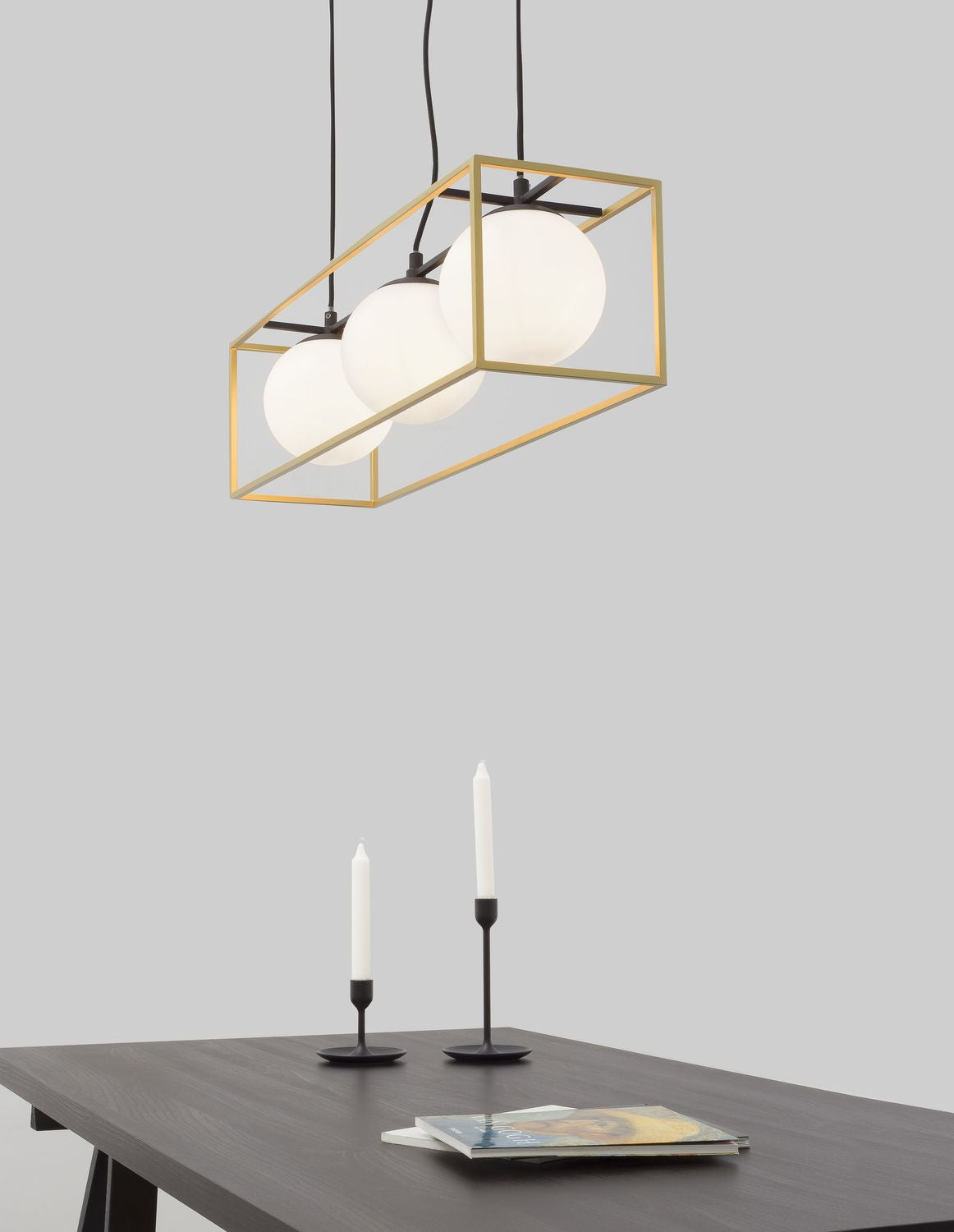 Suspension dorée avec trois globes en verre blanc au-dessus d'une table avec bougies
