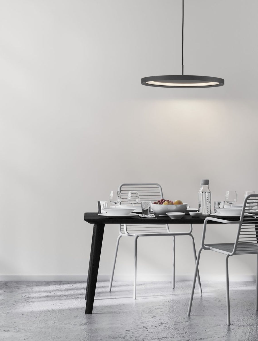 Suspension ronde noire éclairant une salle à manger minimaliste aux murs blancs