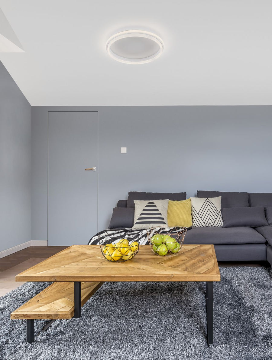 Plafonnier rond blanc allumé au plafond d'un salon gris avec canapé et table basse