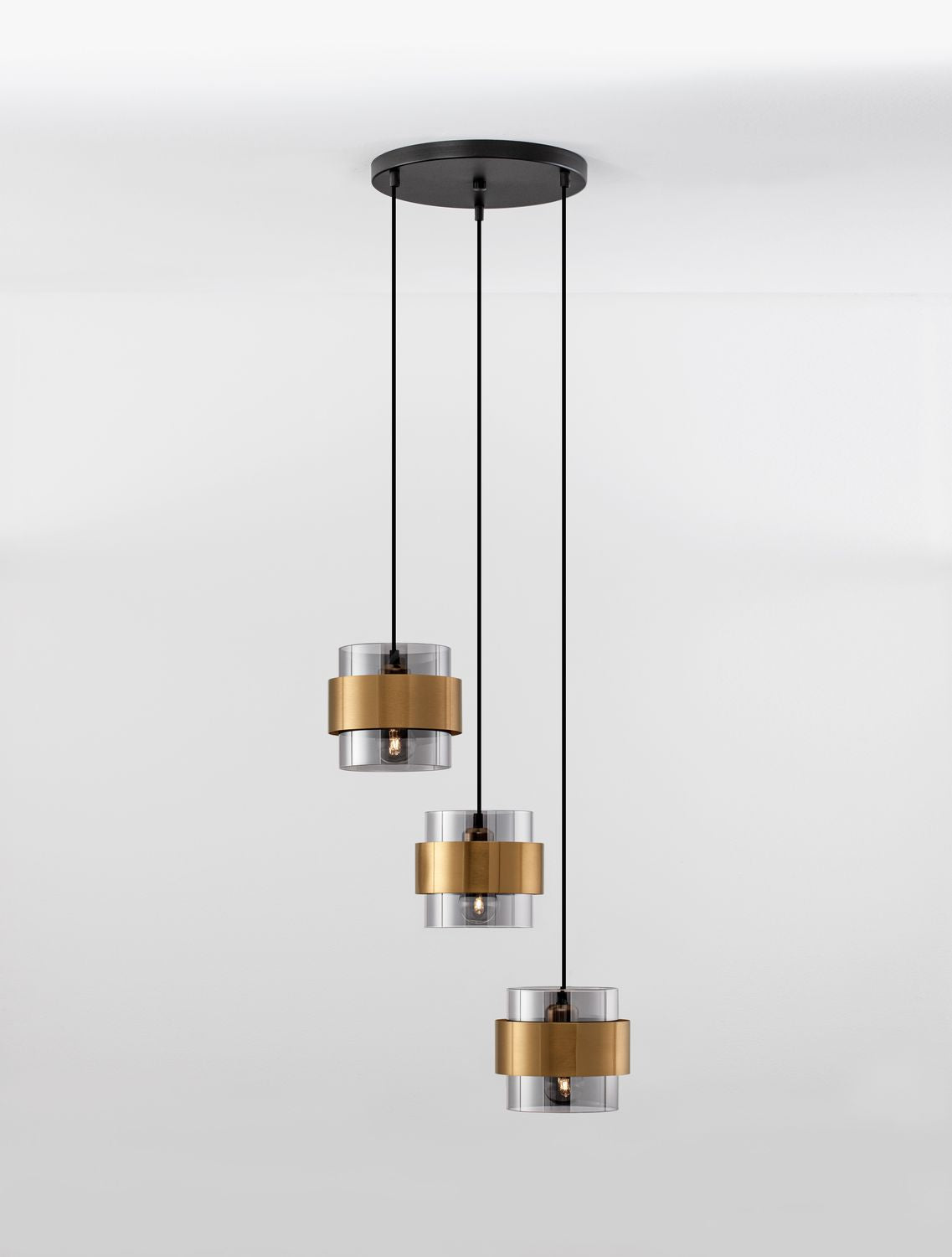 Plan large du trio de luminaires dorés sur fond blanc, câbles tendus verticalement